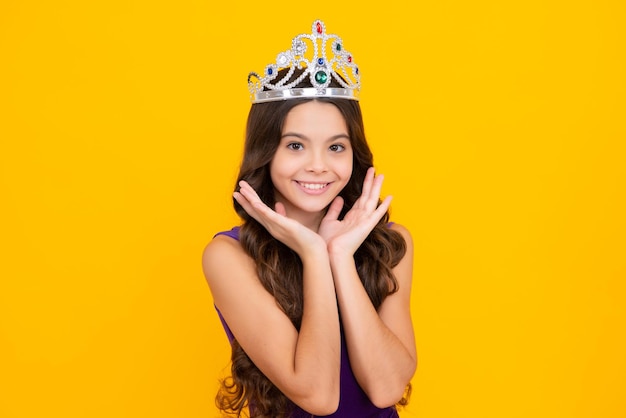 Pequena rainha usando coroa de ouro Princesa adolescente segurando tiara de coroa Conceito de infância de festa de formatura Garota feliz enfrenta emoções positivas e sorridentes