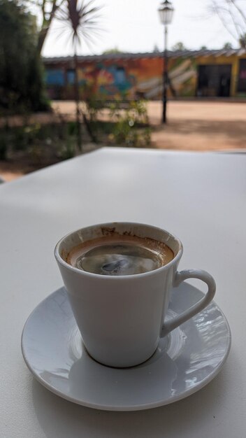 Una pequeña taza blanca de café negro se encuentra sobre una mesa en la terraza