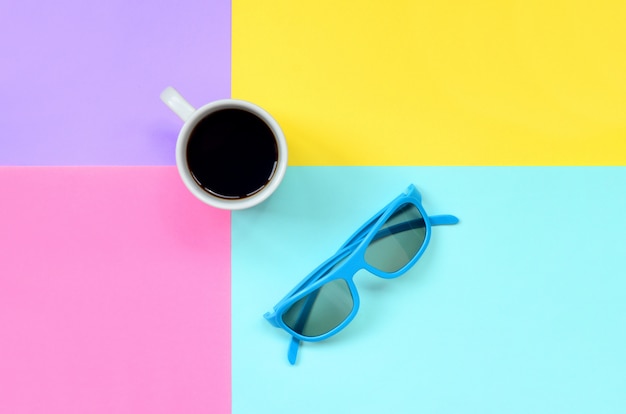 Pequeña taza de café con leche y gafas de sol azules sobre fondo de textura