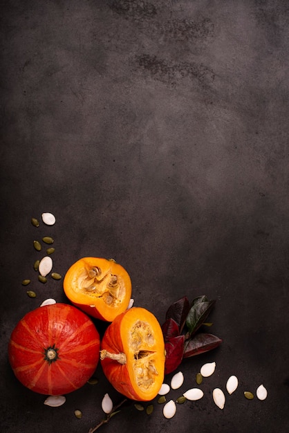 Pequenas abóboras laranja com sementes e folhas de outono em uma mesa escura, vista superior