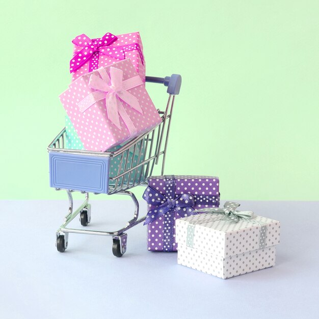 Pequeñas cajas de regalo de diferentes colores con cintas en el carrito de compras en un pastel violeta y azul