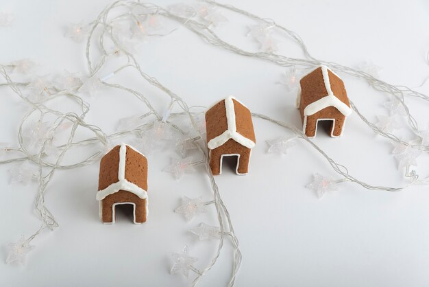 Pequeñas casas de pan de jengibre sobre fondo blanco y guirnaldas navideñas. Productos horneados de Navidad.