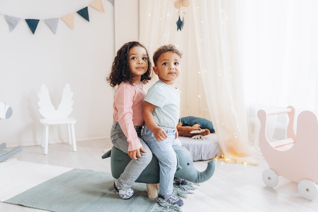 Pequenas crianças afro-americanas, um menino e uma menina estão sentados em uma cadeira na forma de um design de quarto infantil de elefante