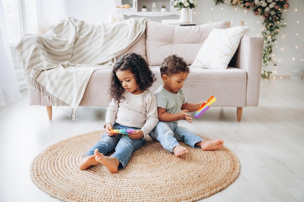 Pequenas crianças negras afro-americanas brincando com brinquedos pop no chão em casa