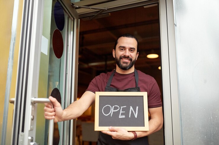 Foto pequenas empresas, pessoas e conceito de serviço - homem feliz ou garçom com palavra aberta no quadro-negro na porta de entrada do bar ou restaurante