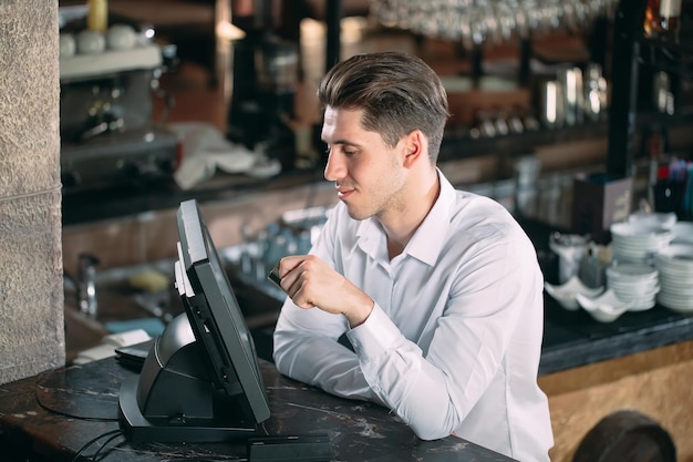 Foto pequenas empresas, pessoas e conceito de serviço - homem feliz ou garçom no avental no balcão com caixa trabalhando no bar ou café.