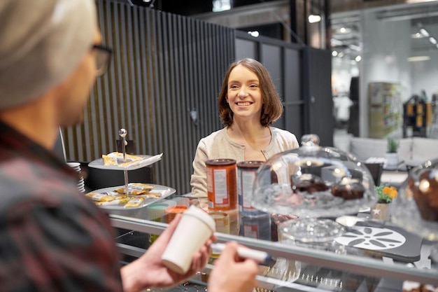 pequenas empresas, pessoas e conceito de serviço - homem ou barman com xícara de café e marcador servindo cliente feminina feliz no café vegan