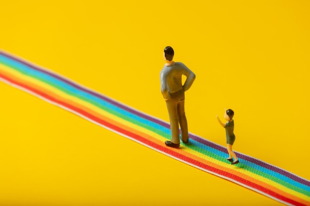 Foto pequeñas figuras de padre e hijo en el camino del arco iris lgbt