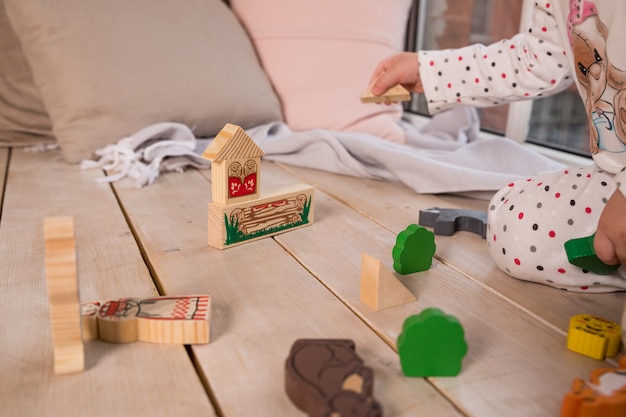 Pequeñas formas de juguete de madera de colores y bloques de construcción en el piso de madera. niña juega con un juego de madera en la habitación de sus hijos en el piso. bloques de colores en el piso.