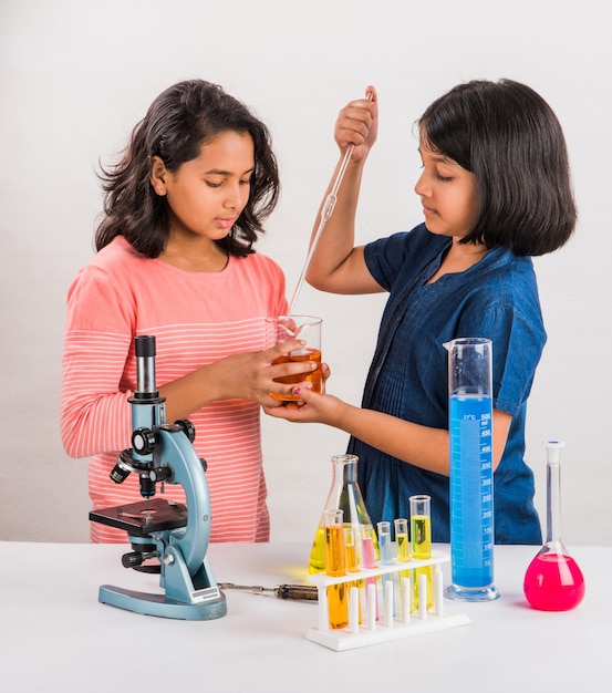 Pequenas garotas indianas curiosas ou cientistas estudando ciências, fazendo experiências com produtos químicos ou microscópio em laboratório, foco seletivo