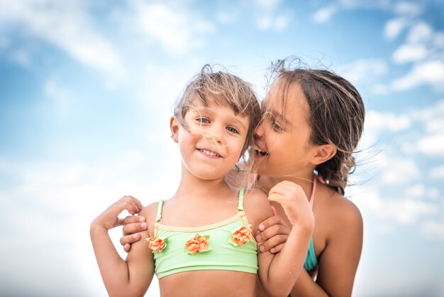 Pequeñas hermanas encantadoras susurran algo en un día de verano