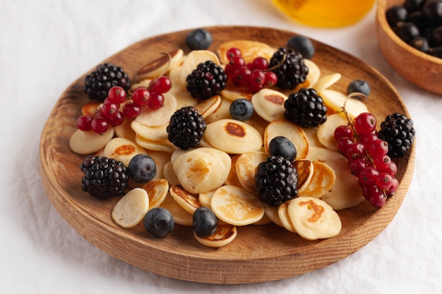 Pequenas panquecas com frutas em close-up numa toalha de mesa branca. Mingau de panqueca. O conceito de tendências de café da manhã no fornecimento.