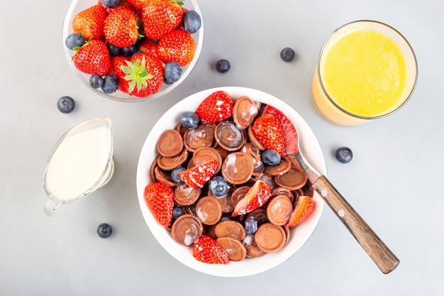 Pequenas panquecas de cereal de chocolate com leite condensado, morango, mirtilo e suco de laranja