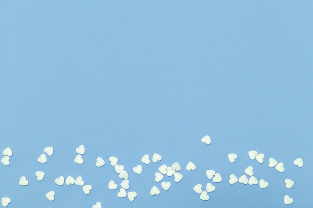 Pequeñas píldoras en forma de corazón blanco sobre fondo azul.