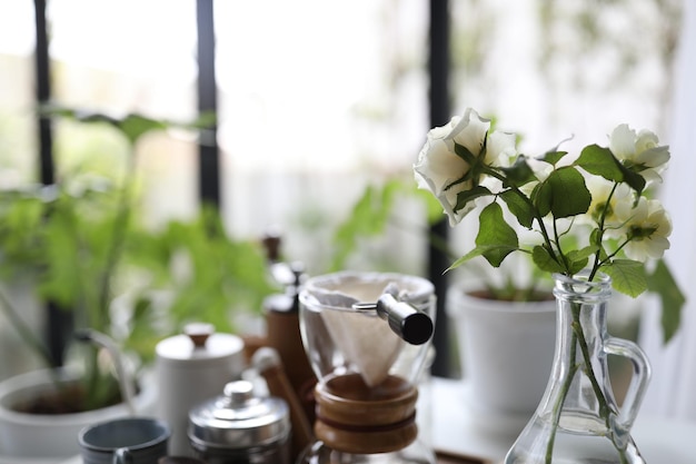 Pequeñas rosas blancas en jarrón de vidrio con café por goteo