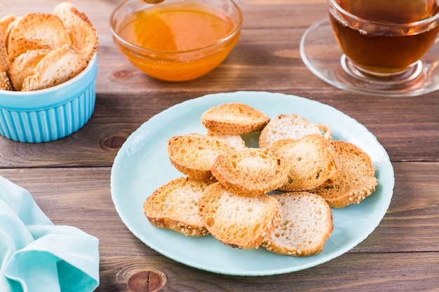 Pequeñas tostadas de pan en un plato sobre una mesa de madera Té casero con miel