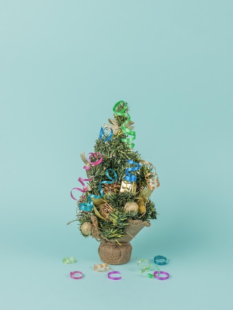 Un pequeño abeto decorado con juguetes y serpentinas sobre un fondo azul. El concepto mínimo del Año Nuevo. Arte contemporáneo. Lugar para el texto.