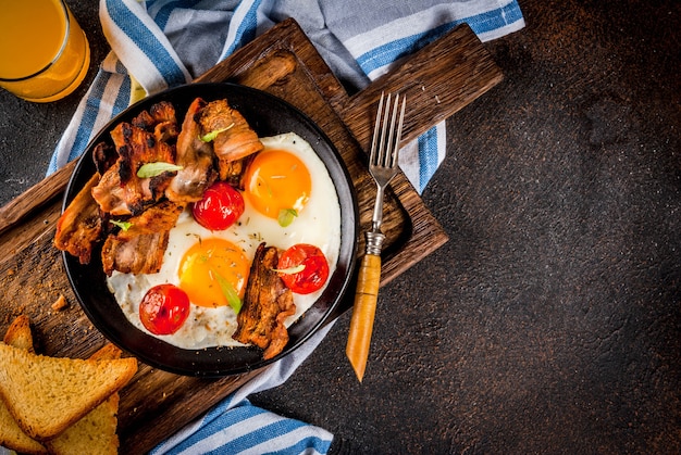 Pequeno-almoço americano inglês caseiro tradicional, ovos fritos, torradas, bacon, com fundo escuro de caneca de café e suco de laranja, espaço de cópia de vista superior