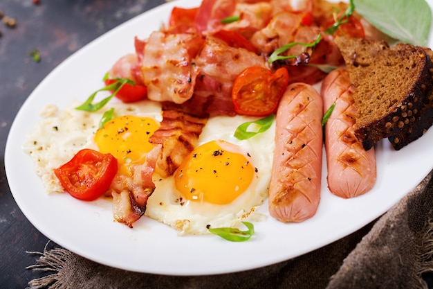 Pequeno-almoço inglês - ovo frito, salsicha, tomate, bacon e torradas.