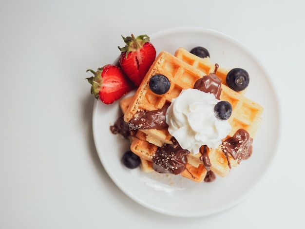 Pequeno-almoço plano leigos. Waffle saboroso com frutas, chocolate e chantilly em uma placa de cerâmica branca