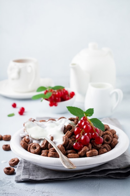 Pequeno-almoço saudável com anéis de milho de chocolate, bagas de groselha, iogurte e chá em um fundo cinza de concreto Copie o espaço.