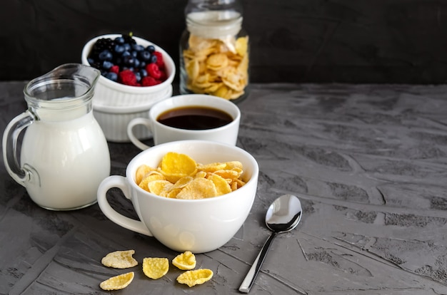 Pequeno-almoço saudável com flocos de milho em um copo branco, frutas, leite e café