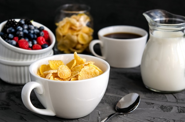 Pequeno-almoço saudável com flocos de milho em um copo branco, frutas, leite e café