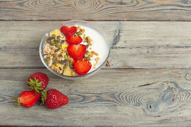 Foto pequeno-almoço saudável com iogurte, frutas e granola na vista superior da mesa de madeira