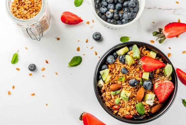 Pequeno-almoço saudável com muesli ou granola com nozes e frutas frescas e frutas morango mirtilo kiwi na vista superior de mesa branca