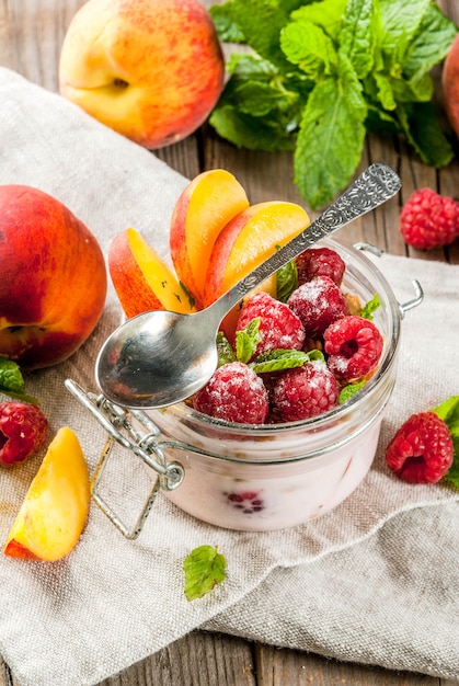 Pequeno-almoço saudável de verão. Pernoite de aveia em uma jarra, granola, nozes, framboesas frescas e pêssego, decorado com folhas de hortelã.