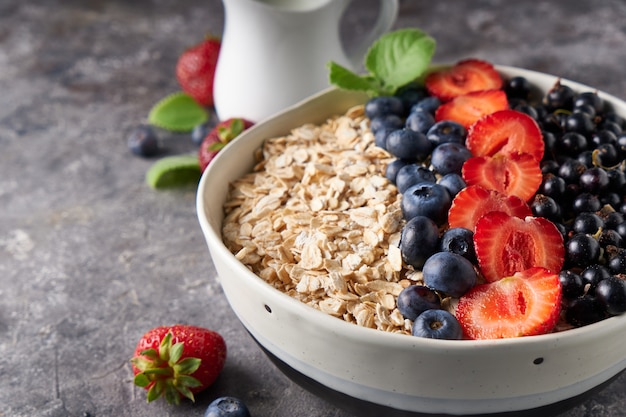 Pequeno-almoço saudável, muesli com passas de Corinto, mirtilos e morangos no choro no espaço escuro