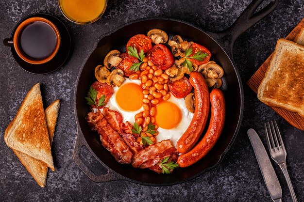 Pequeno-almoço tradicional inglês completo com ovos estrelados, salsichas, feijão, cogumelos, tomates grelhados e bacon.