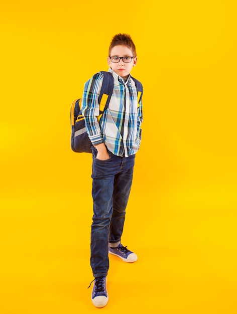 El pequeño alumno con ropa de estilo se para con los brazos cruzados.