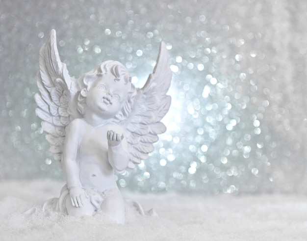 Pequeno anjo da guarda branco na neve em fundo de luzes brilhantes. Decoração de Natal