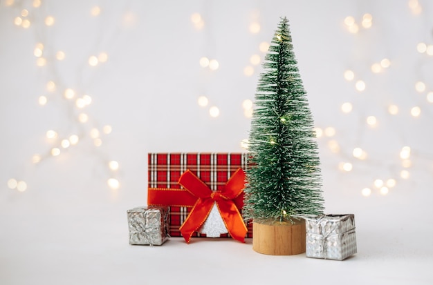 Un pequeño árbol de Navidad artificial con regalos de Año Nuevo sobre un fondo blanco con un bokeh con un lugar para el texto