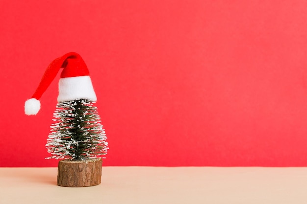 Un pequeño árbol de Navidad con gorro de Papá Noel sobre fondo de color decoración de año nuevo con espacio de copia