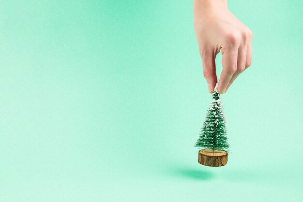 Pequeño árbol de Navidad en mano de mujer sobre un fondo verde. Copie el espacio.