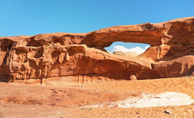 Pequeño arco o pequeña formación de ventana de roca en el desierto de Wadi Rum, el sol brillante brilla sobre el polvo rojo y las rocas, el cielo azul arriba.