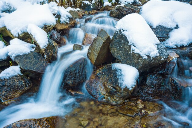 Pequeño arroyo rápido entre pequeñas piedras mojadas y fría nieve blanca en las pintorescas montañas de los Cárpatos en la hermosa Ucrania y su fantástica naturaleza