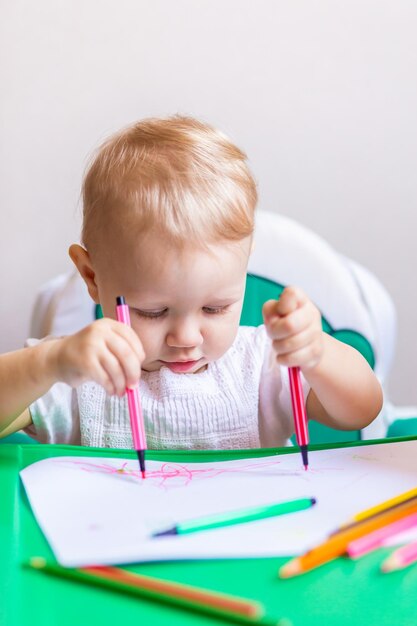 Un pequeño artista lindo dibuja en un álbum con lápices sentado en una mesa pequeña