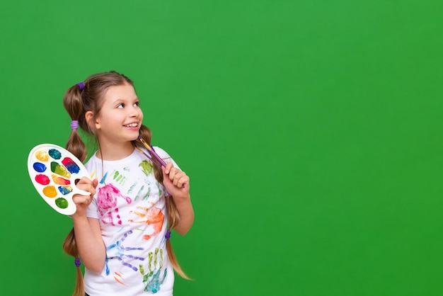 Un pequeño artista con una paleta de colores apunta a su anuncio sobre un fondo verde aislado Cursos de arte para niños