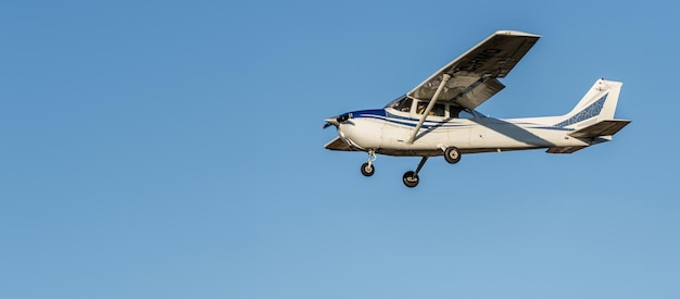 Foto pequeno avião branco com listras azuis de uma hélice cessna voando em um céu azul claro sem nuvens