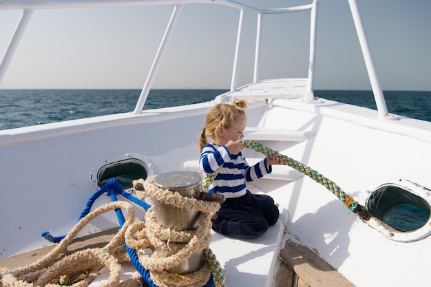 Pequeño ayudante Niño adorable marinero camisa a rayas yate viajar alrededor del mundo Niño lindo marinero ayuda con cuerdas yate proa Aventura niño marinero viajando mar Bebé niño disfruta de vacaciones en crucero