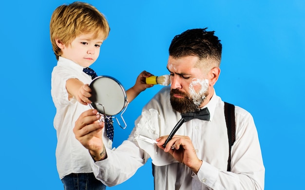 Pequeño barbero. Asistente de papá. Dia del padre. El hijo sostiene el espejo para el padre.