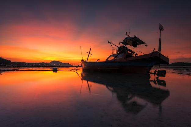 Pequeno barco de pesca com reflexo na praia tópica em phuket