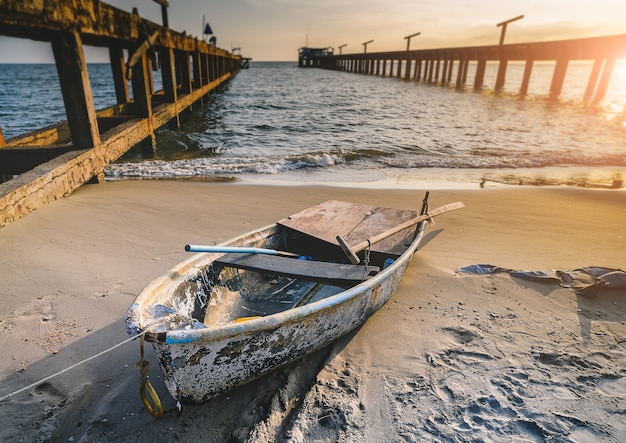 Pequeño barco de madera de pesca en la playa con iluminación al atardecer.