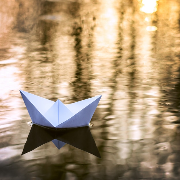 Foto pequeño barco de papel navegando río abajo en otoño al atardecer. concepto de soledad, abandono.