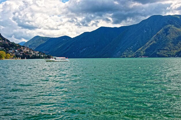 Pequeño barco de pasajeros en el paseo marítimo del lujoso resort en Lugano en el lago Lugano y las montañas de los Alpes en el cantón de Ticino en Suiza.