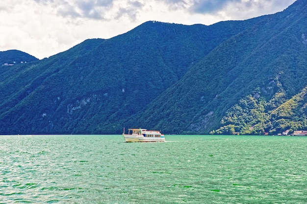 Pequeño barco de pasajeros en el paseo marítimo del lujoso resort en Lugano en el lago Lugano y las montañas de los Alpes, cantón de Ticino en Suiza.