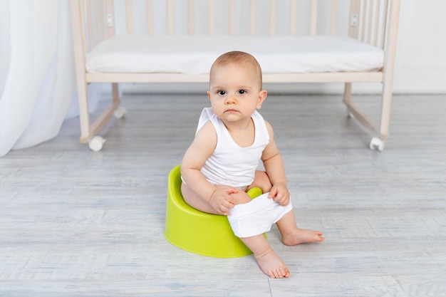 Pequeño bebé de 8 meses sentado en un orinal, inodoro,